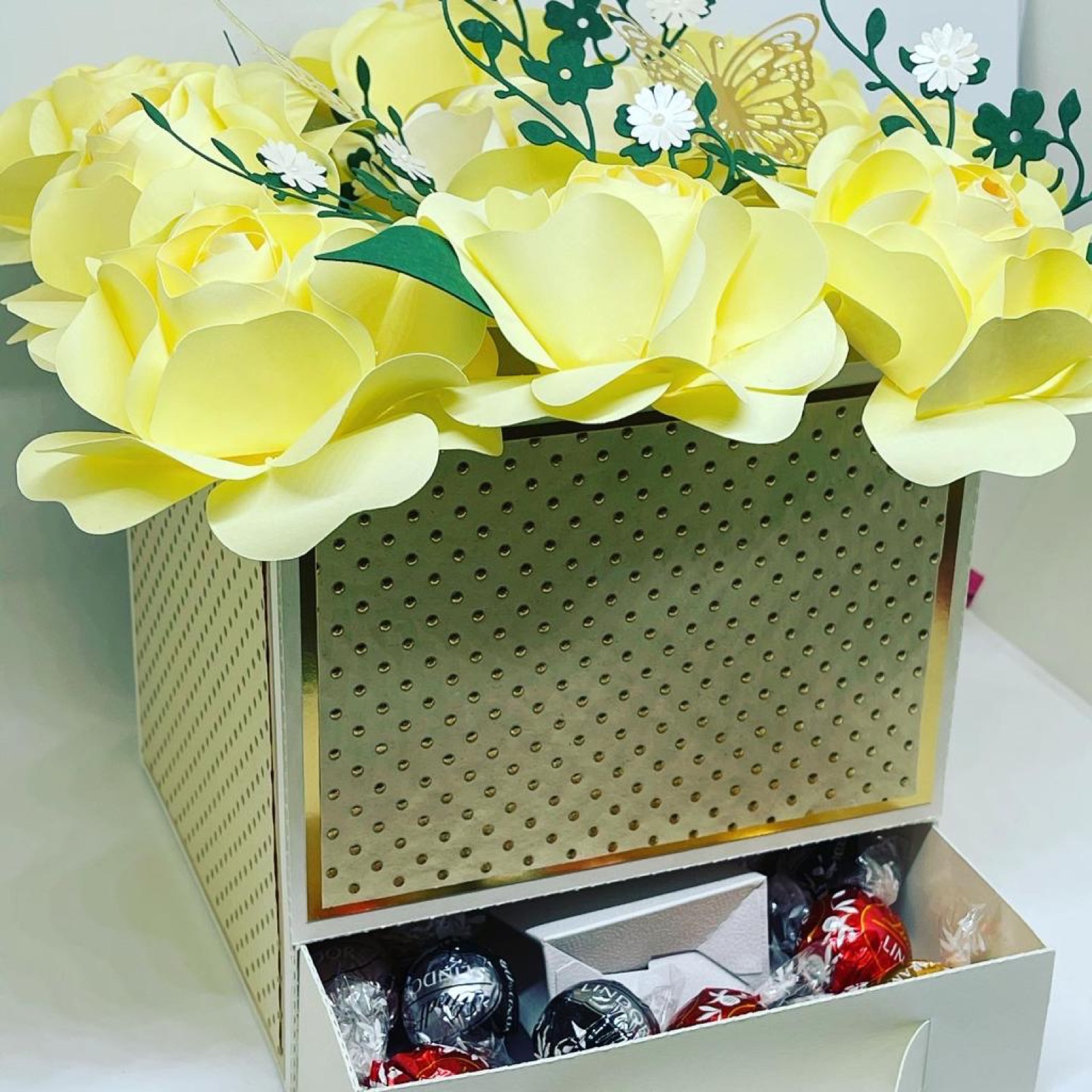 Offene Box mit einem Deckel voller gelber Papierrosen und Pralinen im Innenfach