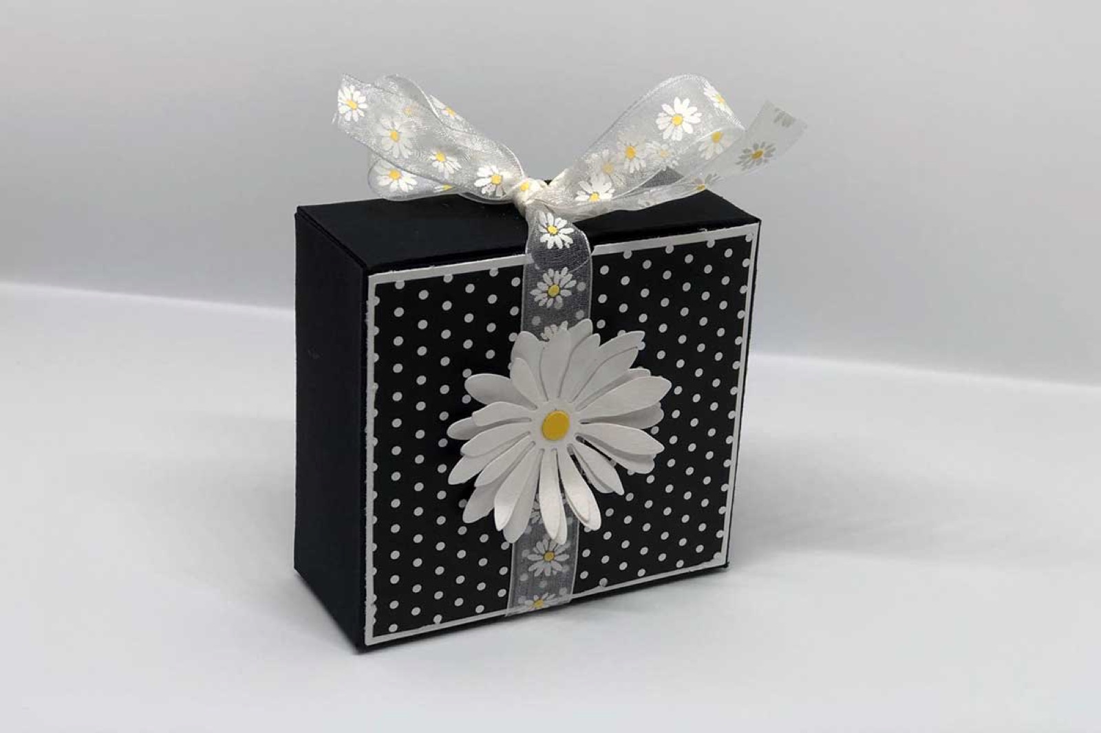 Schwarze Geschenkbox mit weissen Punkten, weisser Papierblume und Schleife