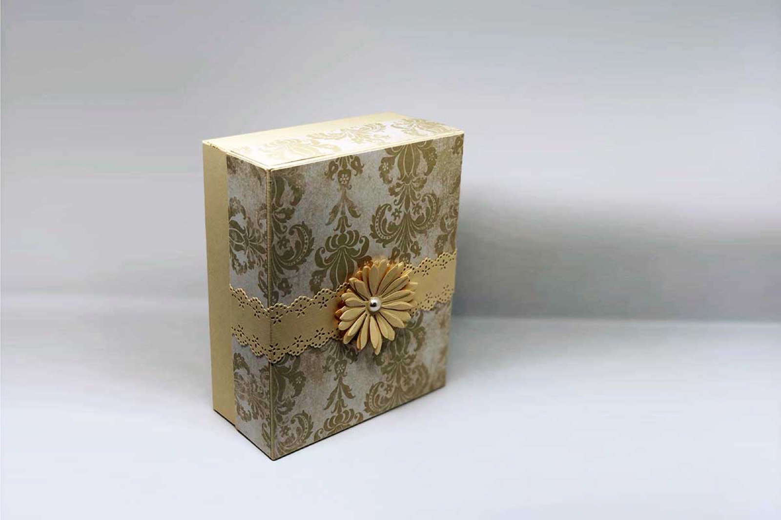 Beige-goldene Box mit antik wirkendem Muster und goldener Rosette
