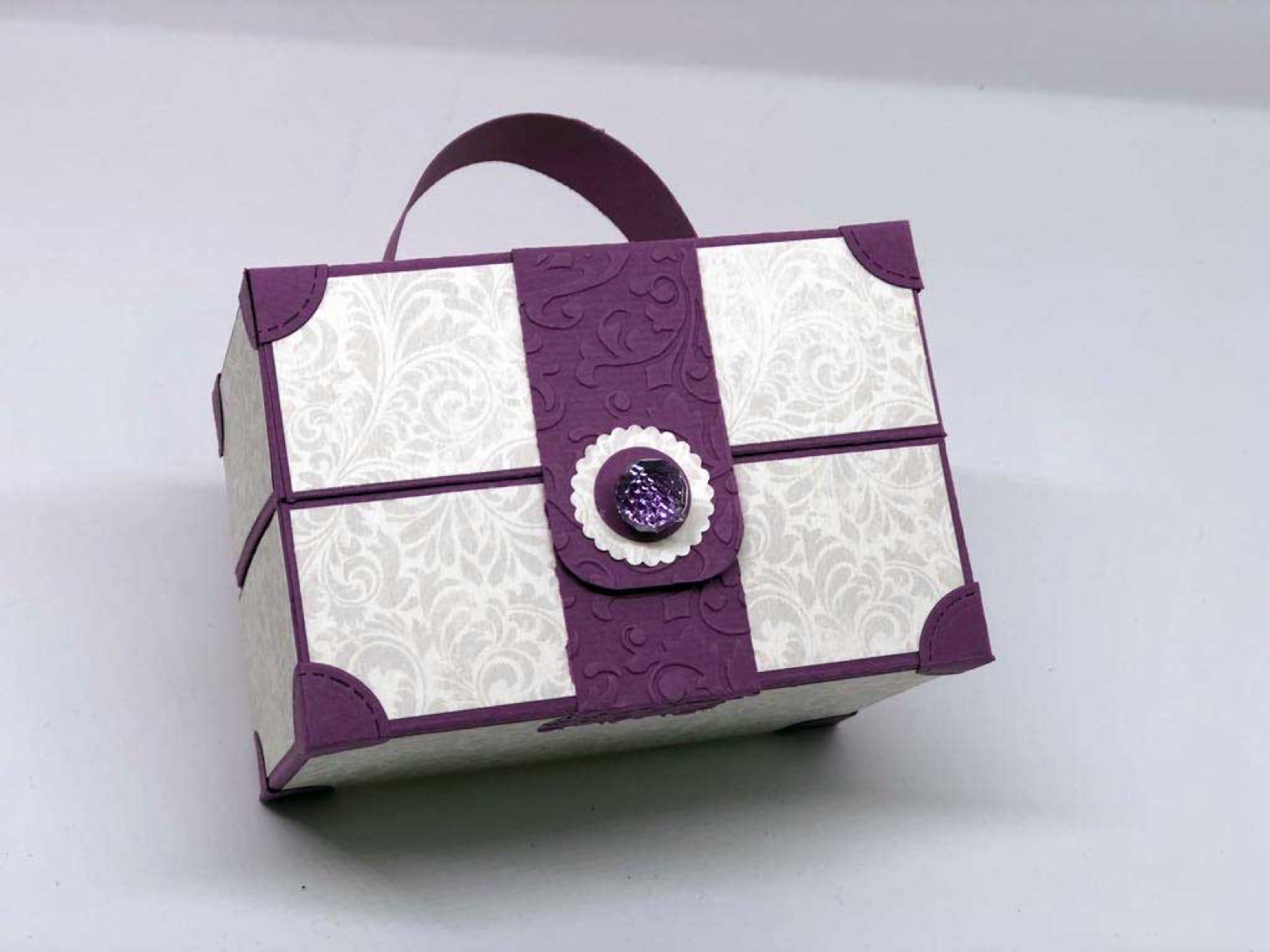 Violett-weisse Box mit Tragegriff und rundem Emblem auf dem Deckel