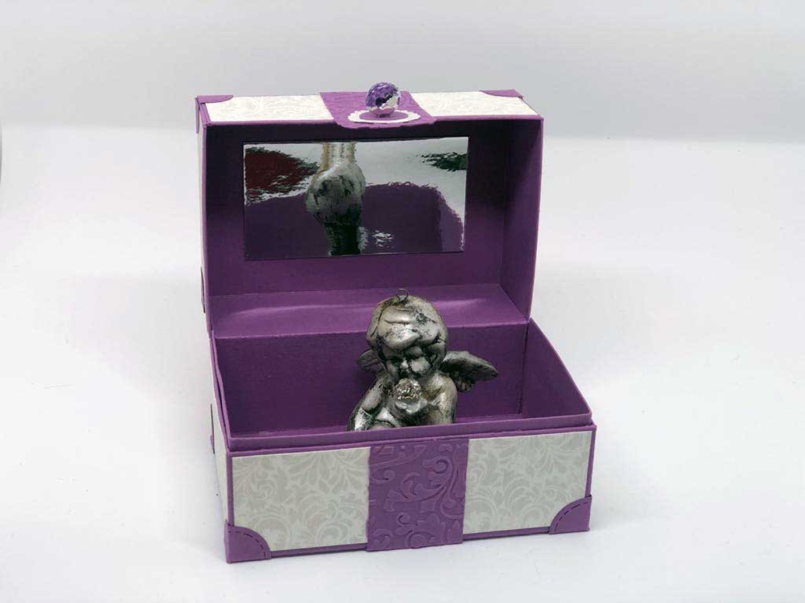 Geöffnete violette Box mit einer silbernen Engelsfigur darin