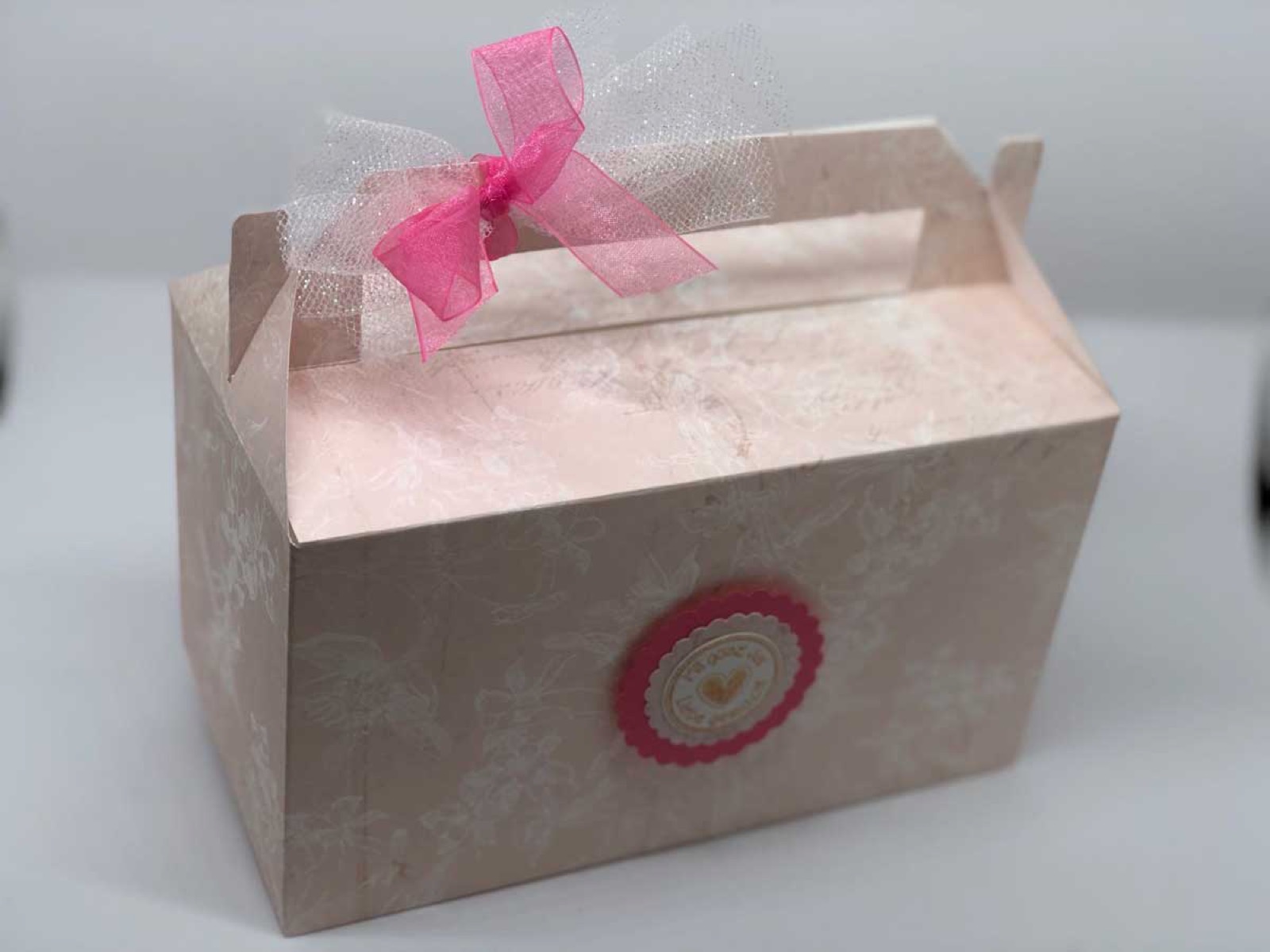 Cremefarbene Box mit Sichtfenster, rosa Schleife und rundem Siegel
