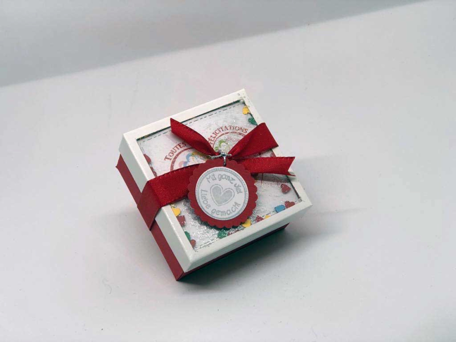 Kleine Box mit Sichtfenster, rotem Band und Papierrosette
