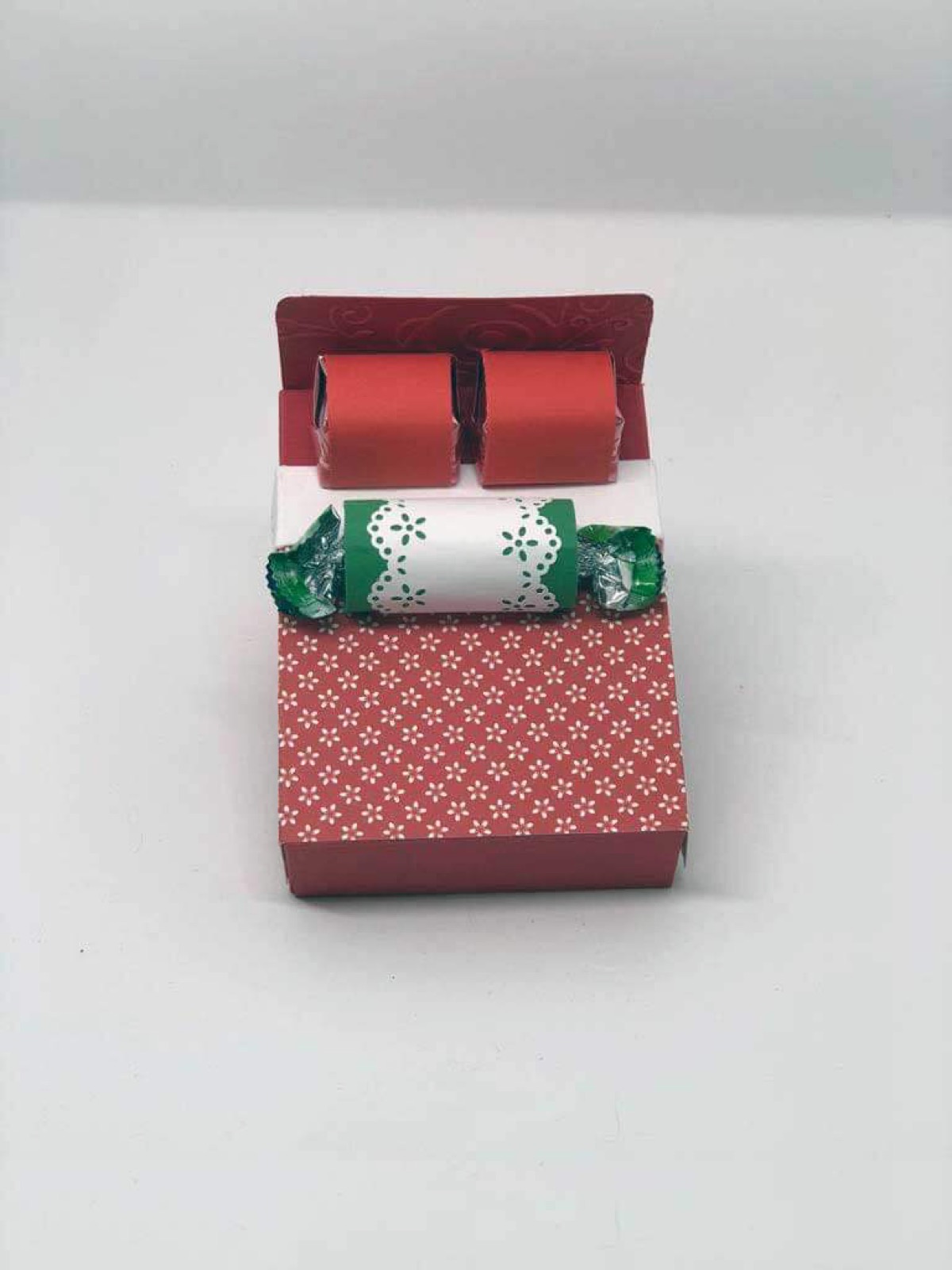 Zwei Mini-Kissen aus rotem und grün gemustertem Papier auf einem Papierbett