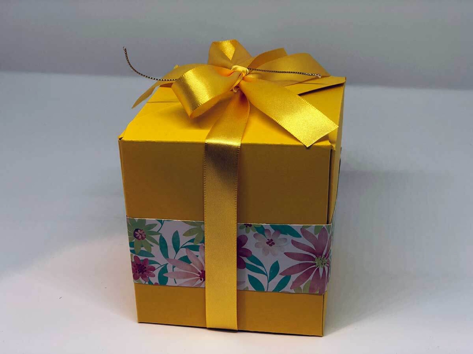 Gelbe Geschenkbox mit goldener Schleife und geblümtem Banderolenband