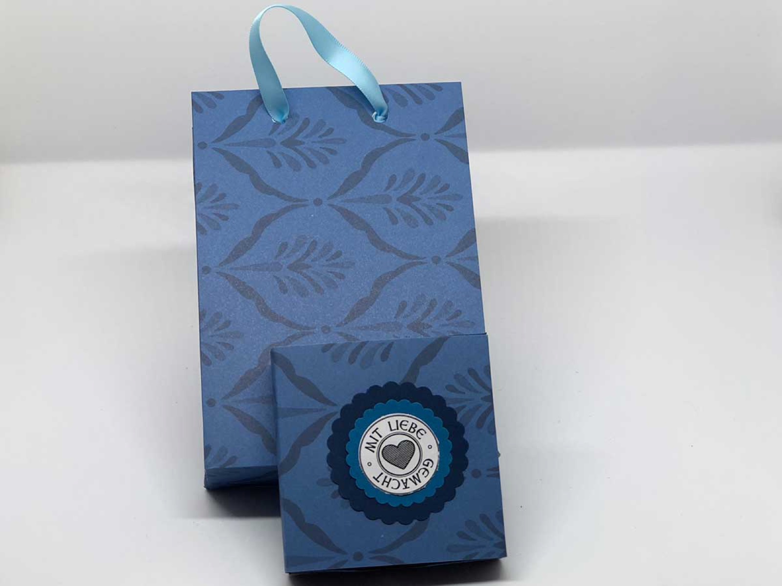Blaue Papiertasche mit geprägtem Muster und kleiner Schachtel davor
