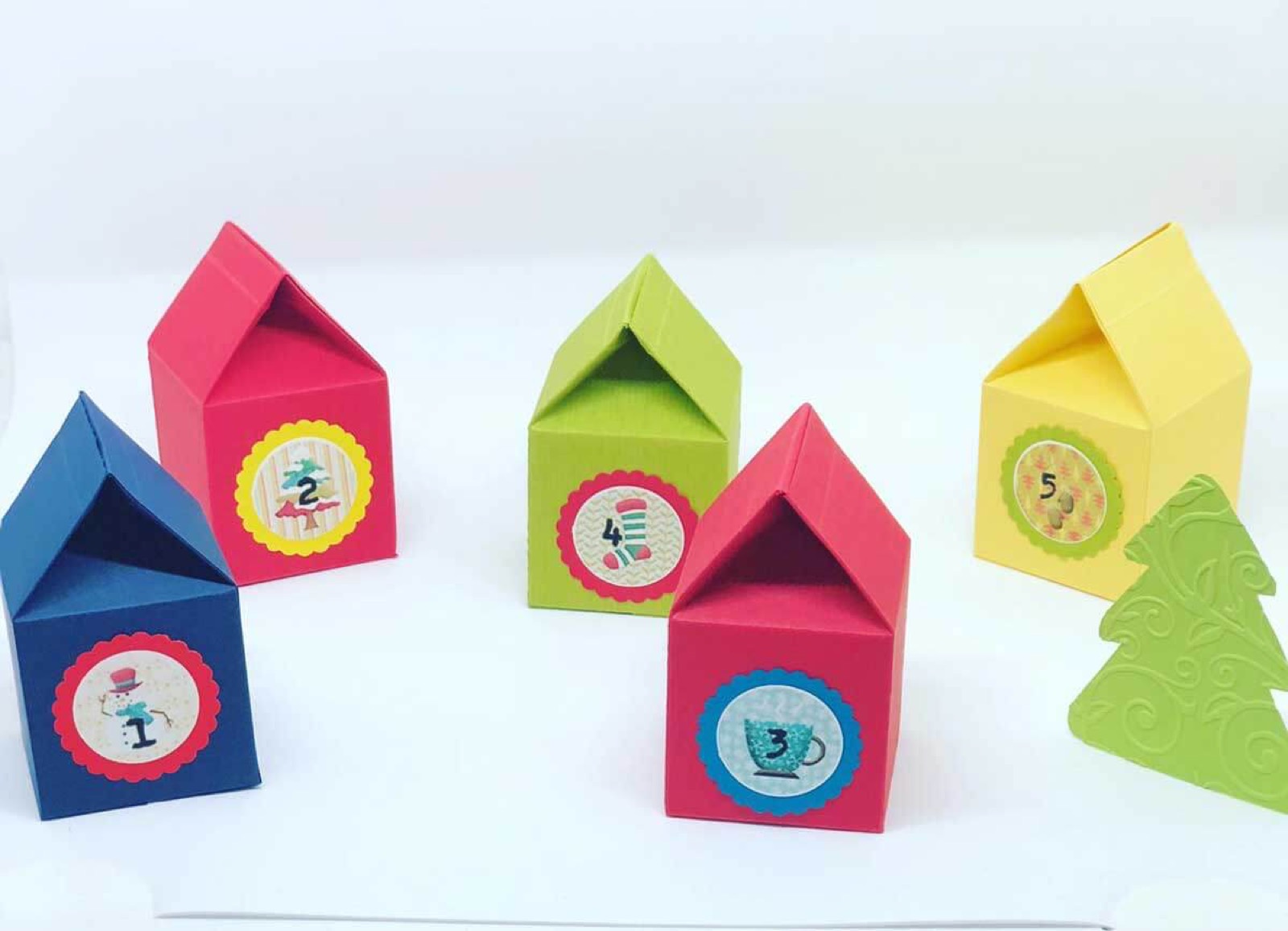 Adventskalender aus bunten Papierhäuschen und kleinen Tannenbäumen