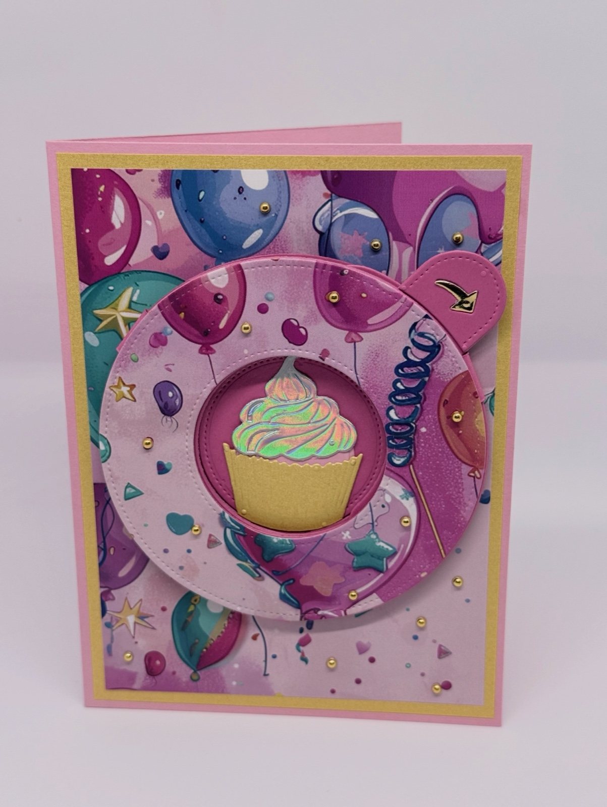 Rosa Geburtstagskarte mit Ballonmuster und geöffneter Drehblende, in der ein Cupcake sichtbar ist