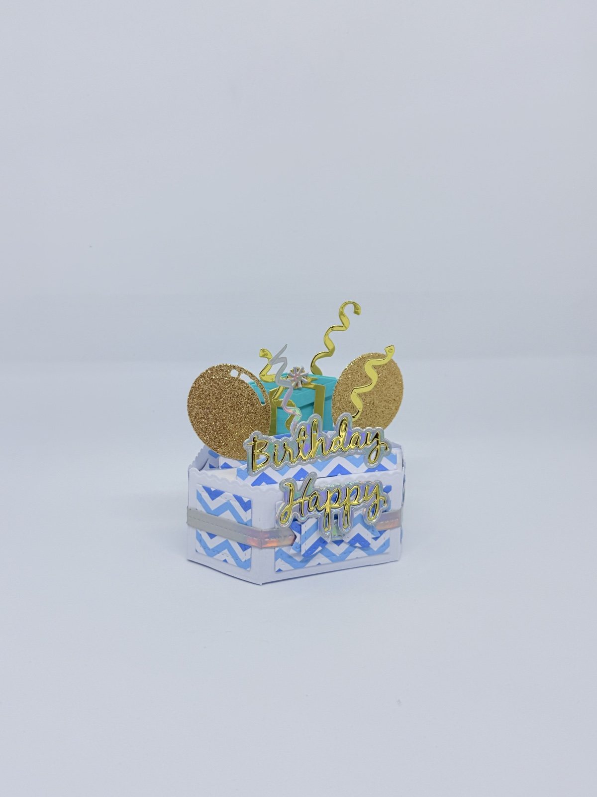 Kleine blau-weisse Geschenkbox mit goldenen Glitzerballons und Schriftzug Happy Birthday