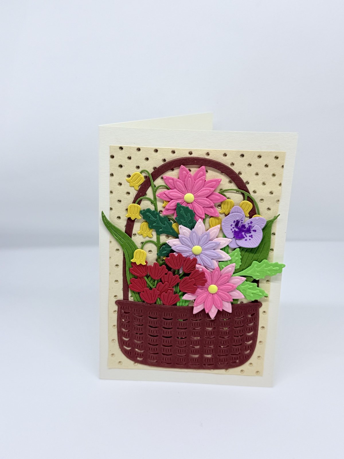 Cremefarbene Karte mit weinrotem Flechtkorb voller bunter Papierblumen