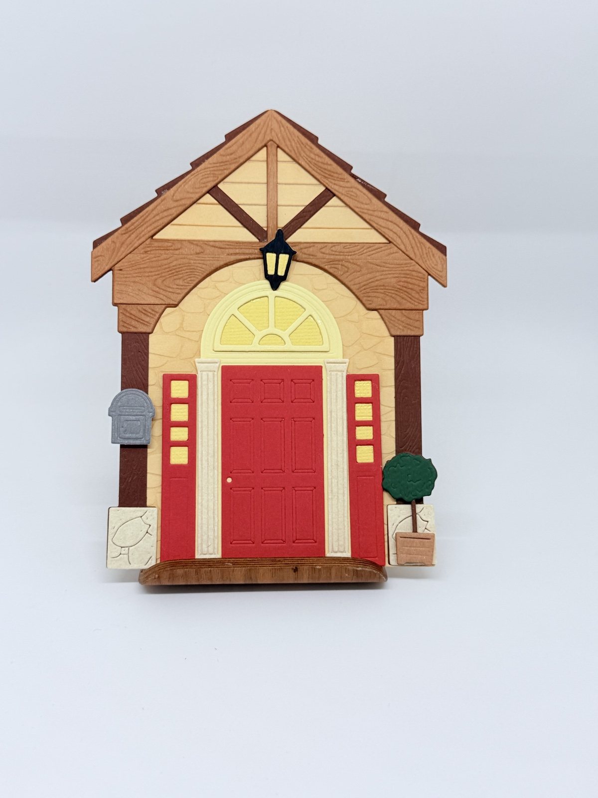 Karte in Form eines Hauseingangs mit roter Tür, Holzgiebel, Laterne und Briefkasten