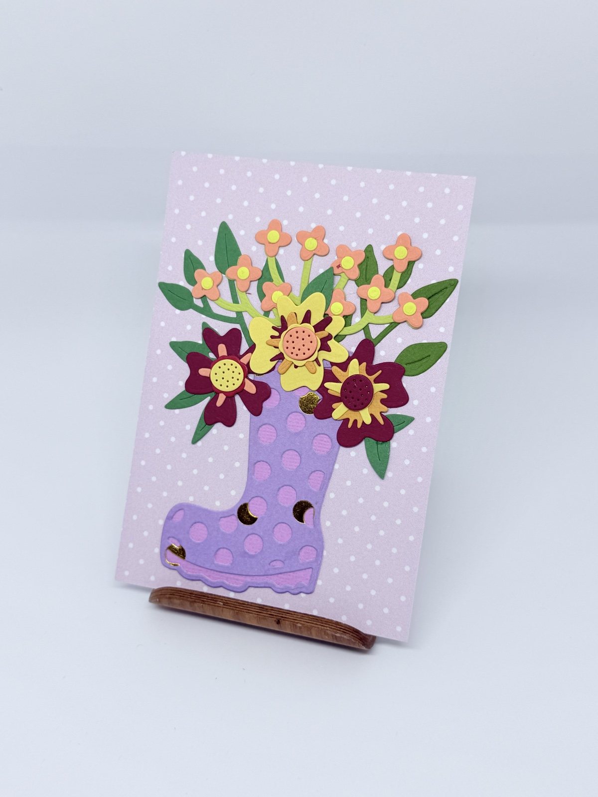Lila gepunktete Karte mit violettem Gummistiefel voller bunter Papierblumen